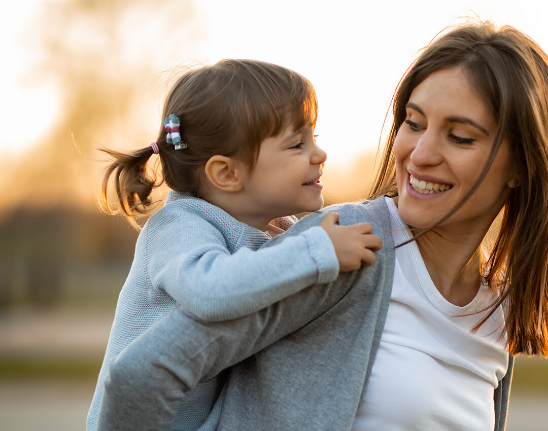 Young daughter on mothers back. Both smiling at each other.